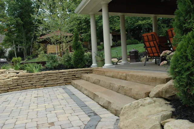 Wide stone slab steps and a dry-laid wall leading from a paver patio to a covered porch